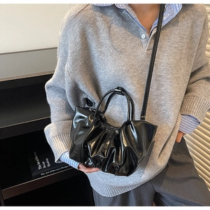 Detail of black glossy pleated cloud bag with elegant top handle and slim shoulder strap