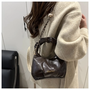 Detail of dark brown glossy patent leather bag with ruched handle and gold chain strap