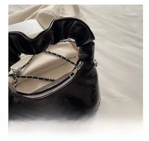 Close-up of smooth silver zipper and glossy pleated leather texture on black handbag