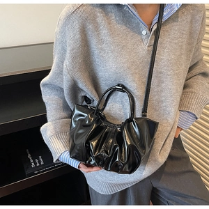Detail of black glossy pleated handbag showing shiny PU leather texture and shoulder strap