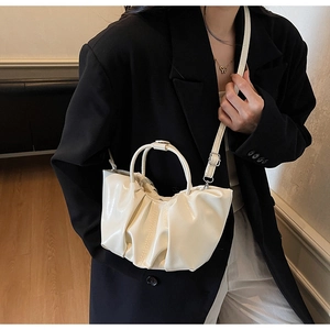 Chic beige pleated cloud bag shown as a crossbody on model in elegant black blazer
