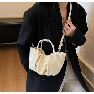 Detail shot of pleated cream cloud bag worn as a shoulder bag in minimalist interior