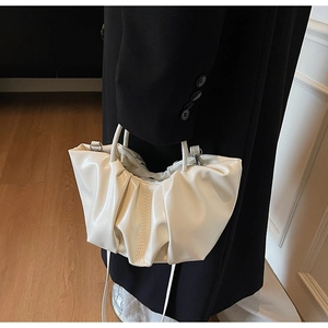 Close-up of pleated cloud handbag with shiny cream leather texture and slim dual handles