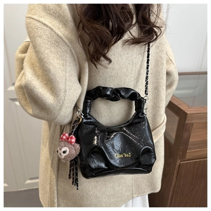 Detail of black glossy pleated leather bag with chain strap and cute bear charm