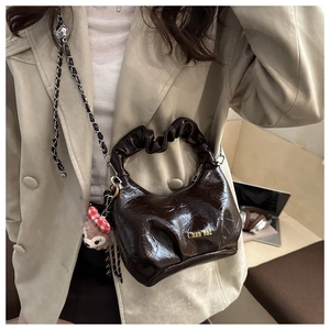 Detail of dark brown pleated leather bag with glossy finish and silver chain strap