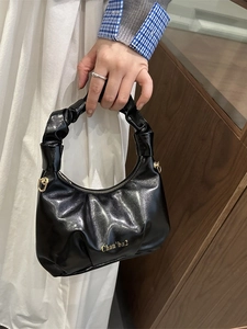 Glossy black pleated handbag with gold hardware and top handle shown in model hand