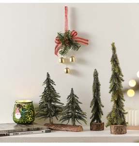 Miniature Christmas trees on wooden bases with festive pine needles and gold bell ornaments
