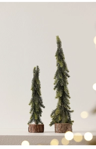 Detail of two mini pine trees with natural wood bases and warm bokeh festive lighting