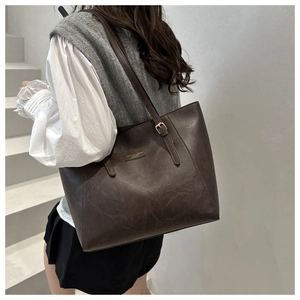 Brown leather tote bag featuring golden buckle strap and logo detail on gray stairs