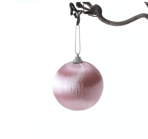 Dettaglio ravvicinato di una pallina di Natale in seta rosa appesa a un ramo rustico