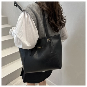 Detail of black leather tote bag showing smooth texture and golden metal hardware accent
