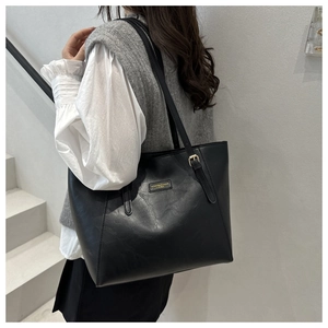 Dettaglio della borsa tote in pelle PU nera con placca logo dorata e trama