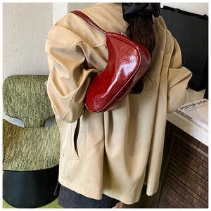 Sac sous le bras en cuir verni bordeaux montré porté à l'épaule en situation