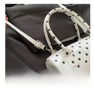 Detail of white patent leather cylinder bag with black polka dots and silver buckle