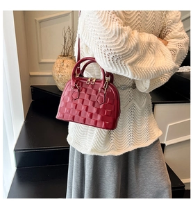 Detail of burgundy shell bag featuring embossed grid texture and golden zippers