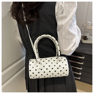 Detailed side view of white polka dot cylinder shoulder bag worn by model in minimalist setting