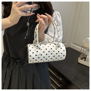 Close-up of white polka dot cylinder handbag featuring double handles and metal zipper detail