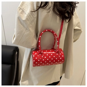 Close-up of a red polka dot cylinder bag with dual handles and slim shoulder strap