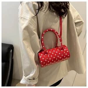 Detailed view of red polka dot cylinder bag with glossy finish and slim shoulder strap