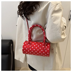 Detailed view of red polka dot cylinder bag with glossy finish and crossbody strap