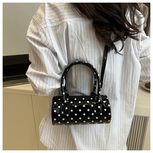 Detailed back view of a small black patent leather cylinder bag with white polka dots