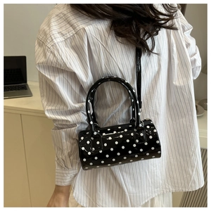 Polka dot cylindrical handbag in shiny patent leather shown with removable shoulder strap