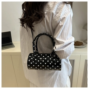 Close-up of a mini black polka dot cylinder bag with glossy finish and crossbody strap