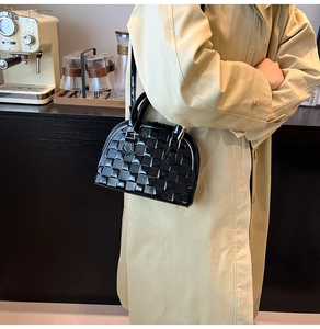 Detail view of a black patent leather shell bag with textured checkerboard embossing