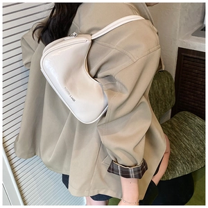 Sac sous le bras beige chic au fini brillant porté par un mannequin en décor moderne