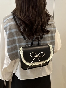 Zaino in pelle nera con pizzo bianco e fiocco indossato da una modella di spalle