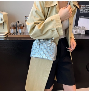 Detail of silver shell bag showing woven texture and metallic finish on a tan trench coat