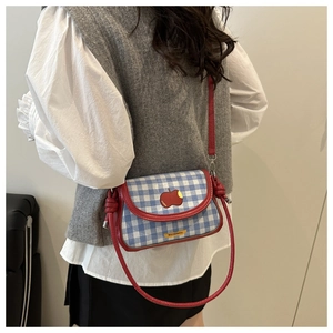 Detail of blue plaid canvas bag with red leather trim and apple patch embroidery