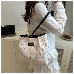 Detail of white tote bag with pink bear prints, gold chain strap and leather logo tag