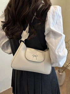 Chic cream white leather underarm bag with a silver bow ornament shown on a model