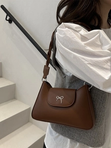 Dark brown leather shoulder bag with a silver metallic bow and braided strap detail