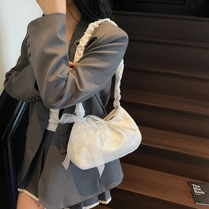 White lace tote bag with bow detail and ruffled strap shown on a gray blazer