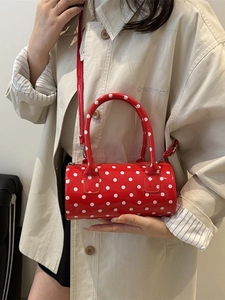 Red cylindrical polka dot handbag with gloss finish and cross-body strap shown on a model