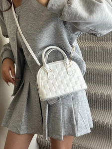 White shell-shaped tote bag with woven texture and gold hardware worn by a model