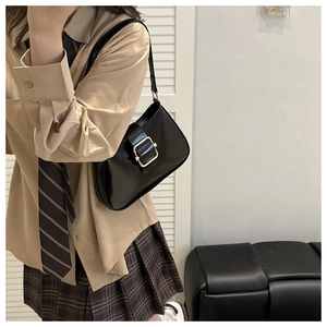 Detail of black glossy leather shoulder bag featuring a vintage golden square buckle