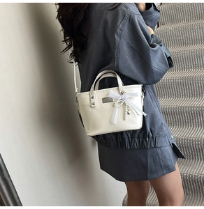 Detail van crème crossbodytas met kanten strik en parelketting aan de schouder