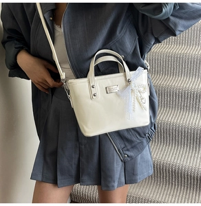 Detail van de crème PU-handtas met parelhanger en elegante zilveren metalen hardware