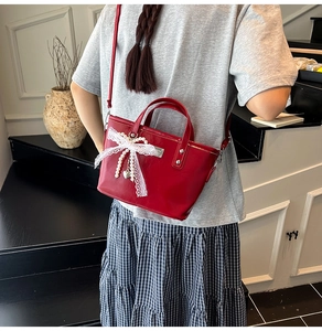 Détail du sac seau rouge avec nœud en dentelle blanche et breloque perle en cœur