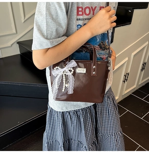 Détail du sac seau marron brillant avec nœud en dentelle et pendentif perle coeur