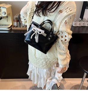 Détail du sac seau noir avec nœud en dentelle blanche et pompons de perles sur un modèle