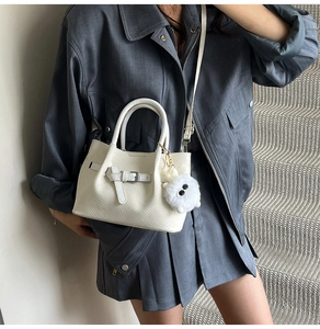 Detail of white woven textured tote bag with stylish plush pendant and long strap