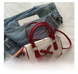 Detail view of a white Boston bag featuring red bows and a heart-shaped metal charm