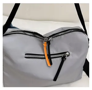 Detail of grey oxford fabric crossbody bag with smooth dual-zipper system and orange puller
