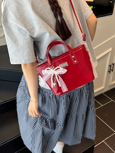 Sac seau en cuir verni rouge avec nœud en dentelle et pendentif perle porté