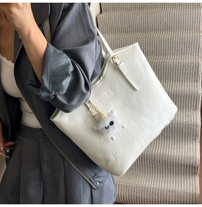 Close-up of white embossed tote bag with butterfly patterns and a plush monster charm