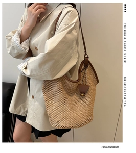 Detail of hand-woven straw tote bag featuring brown leather straps and triangle pendant